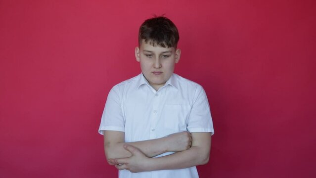 Teenage boy in shirt with short arms shows severe fatigue and desire to sleep, standing in studio on red background.