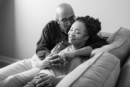 Life style portrait of a black middle aged couple embracing the couch in their living room. This photo is black and white.