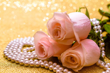 Pink rose and pearl necklace on a shiny gold background
