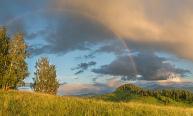 Sunset light and rainbow, rural landscape with hills