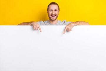 Photo of cheerful positive man with long hairstyle wear gray t-shirt indicating at banner empty space isolated on yellow color background