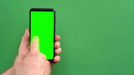 Mobile phone in young man hand. Use smartphone with blank green screen on green color studio background. Male showing black phone with chroma key display. Close up. Mock up of smart phone for Ad, app