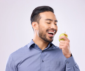 Hungry, eating and an Asian man with an apple isolated on a white background in a studio. Health,...