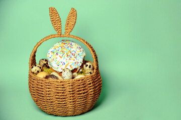 Fototapeta na wymiar Easter decorations in a basket with rabbit ears. Easter cake and eggs on moss, quail eggs and feathers on mint green background. Place for text.