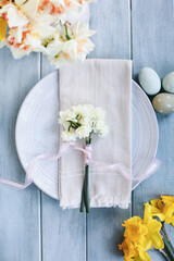 A holiday place setting with plate, eggs, napkin, and daffodils on a blue table decorated for Easter. Shot from flat lay or top view position. Flowers tied with pink ribbon. 