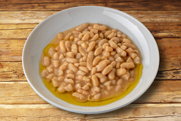 Bean soup seasoned with extra virgin olive oil in a white dish on rustic wooden boards. Clipping path included
