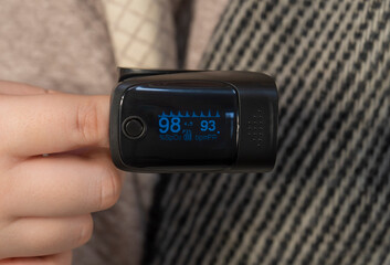 An oximeter is put on a finger (close-up). Measurement of the level of oxygen in the blood. Concept of medicine, healthcare, pharmacy and home treatment