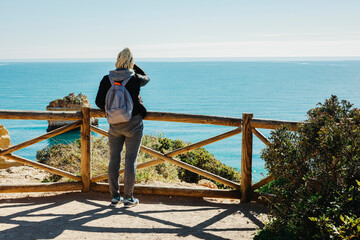 A woman enjoying the ocean view from the top of cliffs at Marinha Beach in Algarve, Portugal