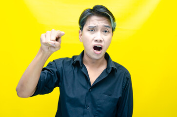 stressed, messed and depressed asian man in black shirt screaming madly and angrily isolated over yellow background.