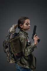 Studio shot of girl teenager survivor with gun and backpack against gray background.