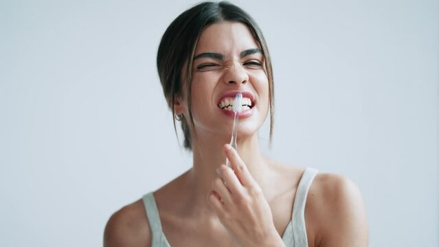 Video of pretty young woman brushing her teeth while looking at camera in the bathroom at home.