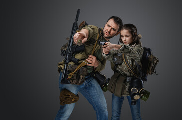 Portrait of man training little girl to shoot handgun in setting of post apocalypse.