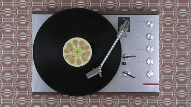 Top view of a spinning vintage record player in front of retro brown wallpaper