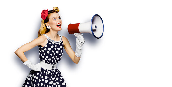 Portrait image of beautiful woman holding mega phone, shout advertising. Pretty girl in black pin up dress, with megaphone loudspeaker. Isolated over white background. Big sales ad.