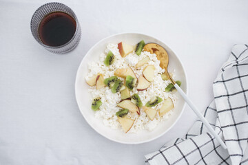 Cottage cheese with fruits, honey in a white plate with a spoon, a napkin, glass of coffee on a white background. Healthy breakfast.