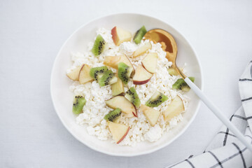 Cottage cheese with fruits and honey in a white plate with a spoon and a napkin on a white background. Healthy breakfast.