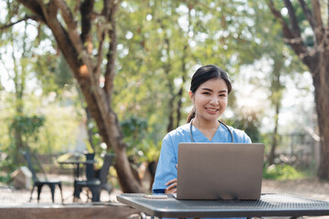 Asian female nurse working outdoor video call with patient online on laptop at desk in park.