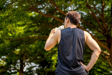 sporty handsome man drinking water after jogging in city public park during summer day, young guy spend quality time on weekend workout outdoor in nature for healthy and active lifestyle