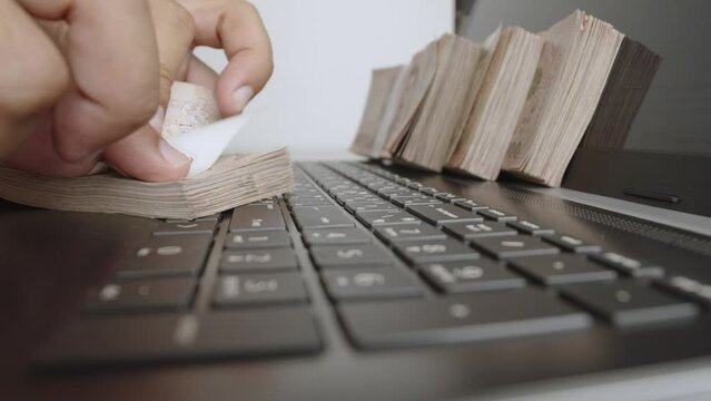 Man hands counting of thousands Thai baht banknotes money and working with laptop or notebook. The baht is the official currency of Thailand.