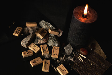 wooden runes on a dark background with a candle and amber stones, for a magical ritual