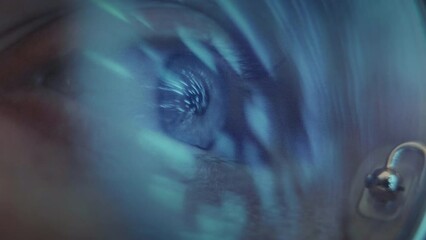 Closeup shot of blue eye, looking at the lights movement across the room late at night. Lights reflection in the computer glasses.