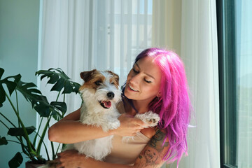 Young beautiful woman with pink hair hugging with her wire haired jack russell terrier at home....