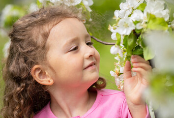 portrait happy little beautiful cute girl smelling flowers of blossoming apple tree. concept of spring mood child, summer. baby summer time. allergy to bloom