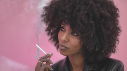 Naklejka premium Young attractive African woman with happy cheerful smile smoking in a studio