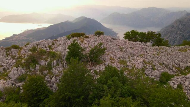 The stunning beauty of the Boka-Kotor bay is captured in this drone footage. The drone glides past a rock, revealing the magnificent panorama of the bay at sunset. This stock video is perfect for any