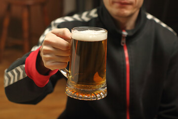 a young man holds a full mug of beer in his hand