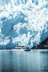 Vertical shot of a huge ship swimming in the sea with an icy glacier in the background in Alaska