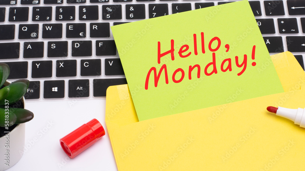 Poster text hello, monday is written in red marker on a yellow card. in the frame is a laptop keyboard on w