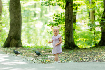 Naklejka premium cute little girl in a purple muslin dress walks in the park in the woods in summer.Earth Day. Children Protection Day
