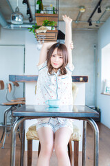 朝、パジャマ姿でイスに座って腕を伸ばしている若い女性