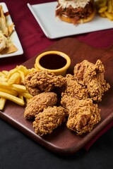 Close up fried chicken wings and a side of fries on a wooden cutting board with a dipping sauce