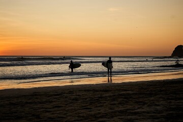 Fototapeta na wymiar People walking along a sandy beach, each carrying a long surfboard in their hands