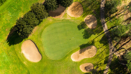 Aerial perpendicular view of an empty golf course with green hills and sand bunkers. The sports...