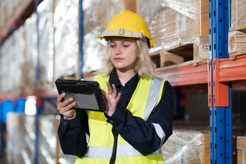 Female warehouse worker working at work checks stock, inventory with tablet on shelf pallet in the...
