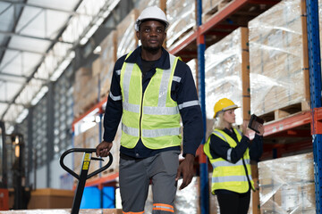 African American male warehouse worker pushing load cart in storage warehouse. Male warehouse worker moving boxes of products at distribution branch .Inspection quality control