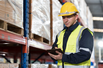 Male warehouse worker working at work checks stock, inventory on shelf pallet in the storage warehouse. Warehouse worker working in warehouse