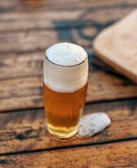 Vertical shot of a glass of foamy beer on a wooden beach table