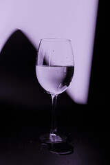 A glass glass with drops of water on a dark background with a purple glow