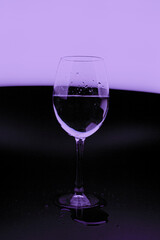 A glass glass with drops of water on a dark background with a purple glow