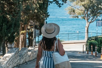 Fototapeta premium Woman wearing a striped sundress and carrying a beach bag, walking toward the sea