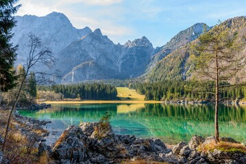 Scenic view of Lake Fusine with shallow water surrounded by trees and rocks against steep mountains
