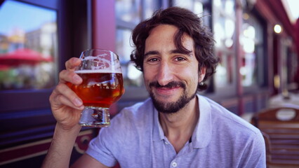 Happy person drinking beer outdoors smiling at camera. Portrait of one young man holding glass of...