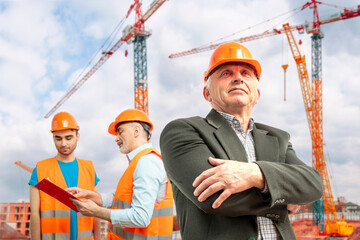 Older construction supervisor with younger worker helper at construction site. Managers wearing...