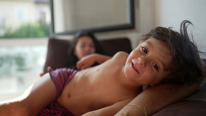 Cute little boy lying on mother body. Shirtless small kid in morning weekend leisure