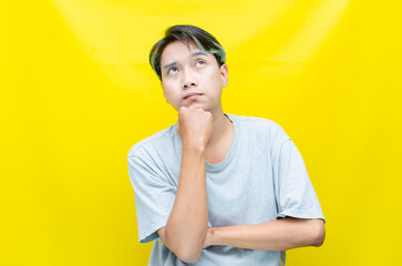 Thoughtful confused asian man thinking and wondering to choose something isolated over yellow...