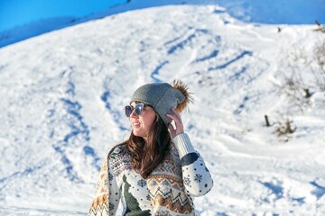 Fototapeta na wymiar Female tourist with sunglasses and a scarf admiring the beautiful view on a snowy mountain